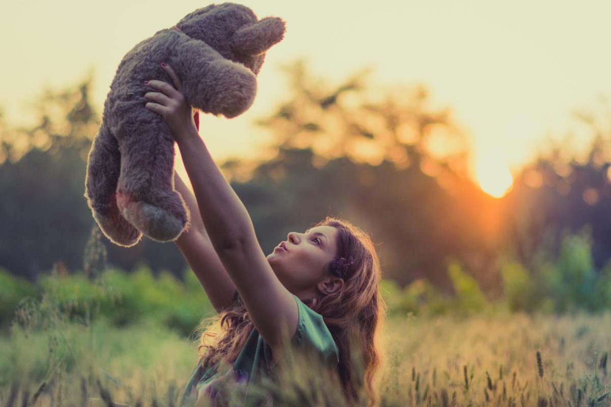 Girl holding teddy bear up to they sky at sunset